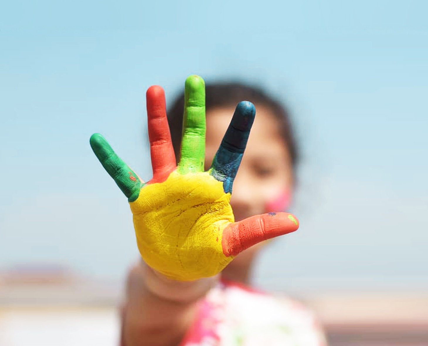 Early childhood care and education. Robert Wood Johnson Foundation. young girl holding a colorful painted hand in front of her face 