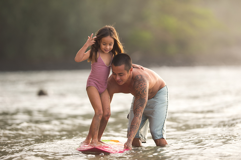 Father teaches daughter to surf in shallow water